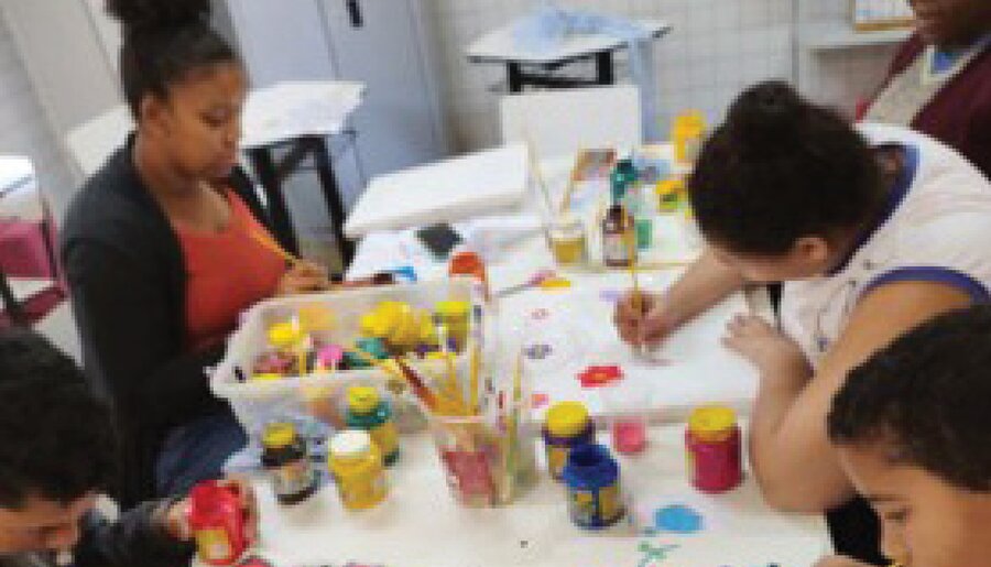 Crianças pintando em atividade acompanhada por educadoras na Associação Pestalozzi de Cuiabá